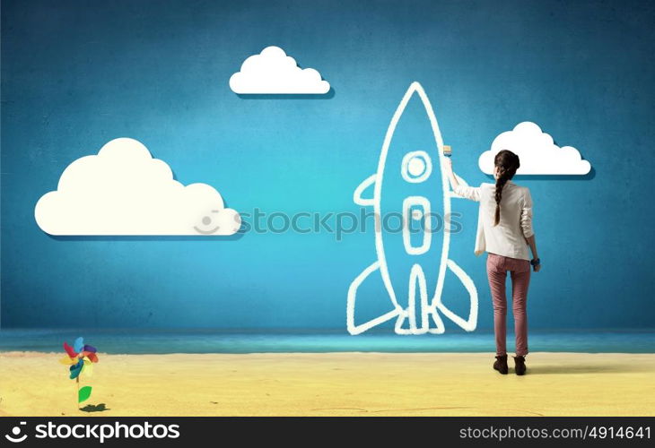 Girl drawing rocket. Young student girl standing with back and drawing rocket