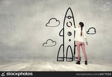 Girl drawing rocket. Young student girl standing with back and drawing rocket