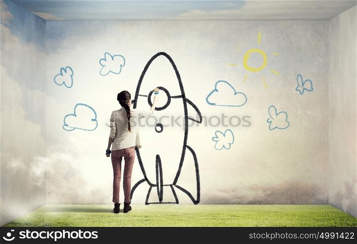 Girl drawing rocket. Young student girl standing with back and drawing rocket