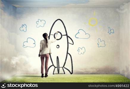 Girl drawing rocket. Young student girl standing with back and drawing rocket