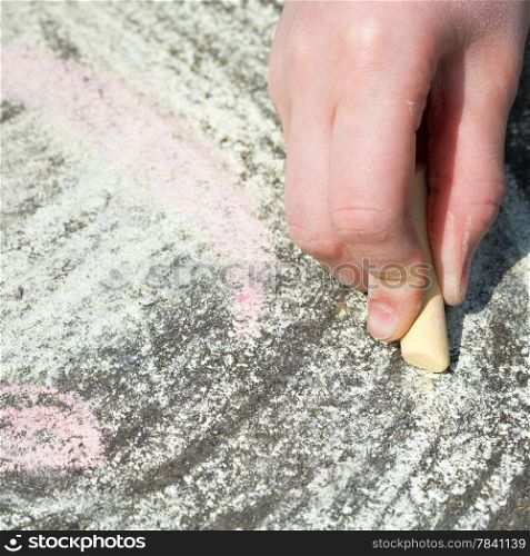 girl drawing with colored chalk on pavement on street close up