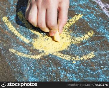 girl drawing yellow sun in blue sky with colored chalk on pavement on street