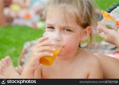 Girl drinking fruit juice from a plastic disposable cup and looked into the frame