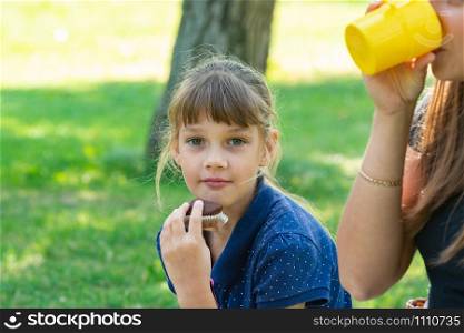 Girl eating a cupcake on a picnic, next to a girl drinking tea