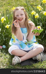 Girl Eating Chocolate Egg On Easter Egg Hunt In Daffodil Field