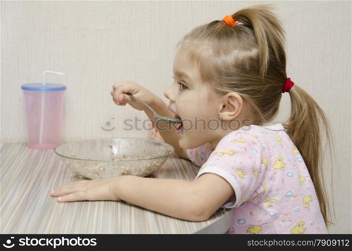 Girl eating porridge sitting at the table. The profile view. Home furnishings