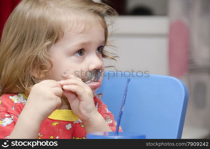 girl eats a cake sitting at the table. Passionately licks spoon and looks right. Home furnishings