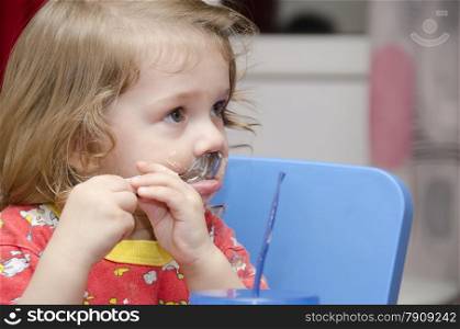 girl eats a cake sitting at the table. Passionately licks spoon and looks right. Home furnishings