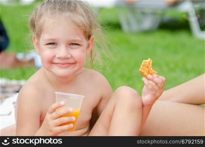 Girl eats cookies, drinks juice from a plastic disposable cup and smiling looked into the frame
