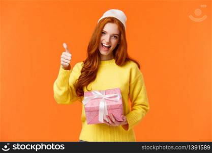 Girl enjoying holidays, got super cool present. Cheerful and upbeat good-looking redhead woman in yellow sweater, winter white beanie, show thumb-up in yes, approval or like gesture, smiling.. Girl enjoying holidays, got super cool present. Cheerful and upbeat good-looking redhead woman in yellow sweater, winter white beanie, show thumb-up in yes, approval or like gesture, smiling