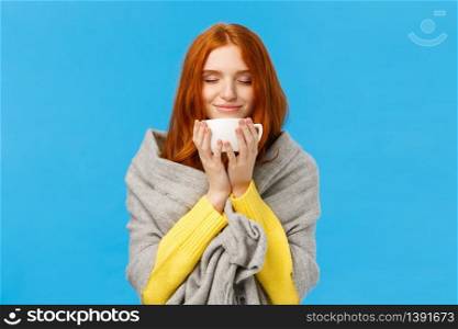 Girl enjoying nice hot cup of coffee smelling flavour with closed eyes and delighted, pleased smile, wrapping herself warm grey scarf, warming during winter low temprature weather, blue background.. Girl enjoying nice hot cup of coffee smelling flavour with closed eyes and delighted, pleased smile, wrapping herself warm grey scarf, warming during winter low temprature weather, blue background