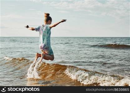 Girl enjoying sea jumping over waves spending a free time over sea on a beach at sunset during summer vacation. Girl enjoying sea jumping over waves spending a free time over sea on a beach during summer vacation