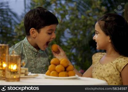 Girl feeding her brother a laddoo