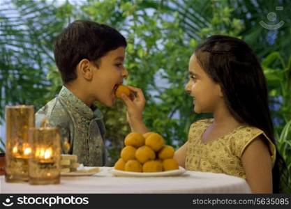 Girl feeding her brother a laddoo