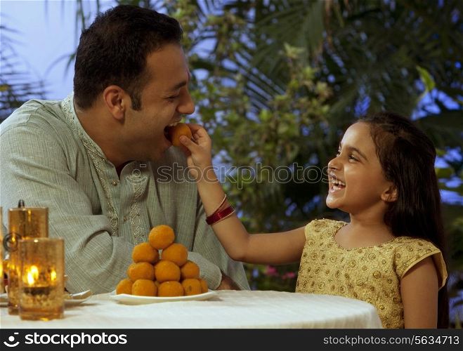 Girl feeding her father a laddoo