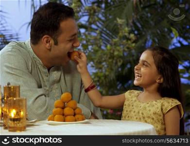 Girl feeding her father a laddoo