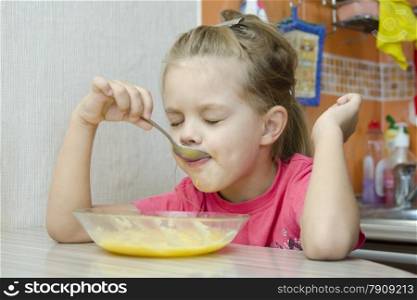 Girl five years eats porridge, sitting at the kitchen table.