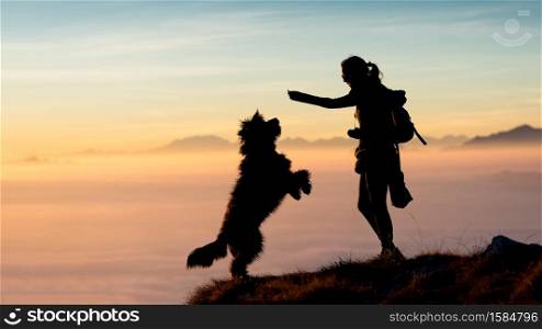 Girl gives food to his mountain dog photo silhouettes with a spectacular backdrop of clouds and mountains