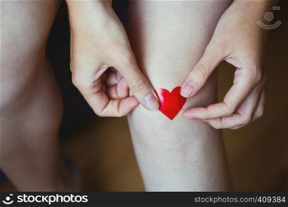girl glues medical plaster in the form of a red heart on the leg