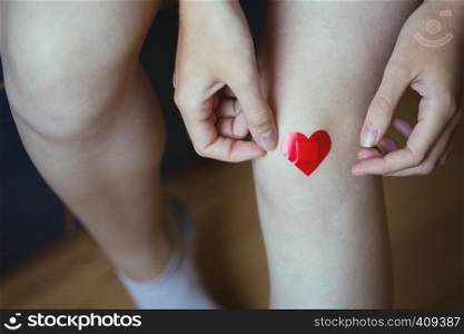 girl glues medical plaster in the form of a red heart on the leg