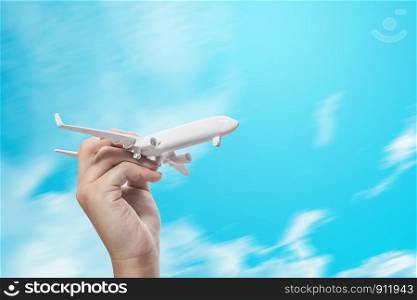 girl hand holding white model plane on blue sky, concept of worldwide travel