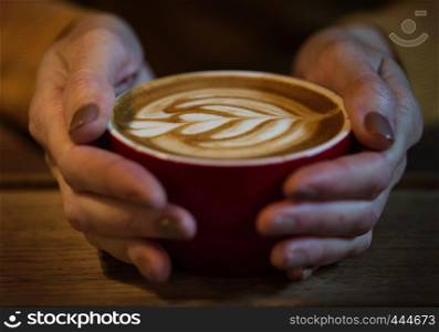 girl hands holding a red cup of capuccino
