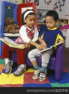 Girl Helping Boy Read In Classroom