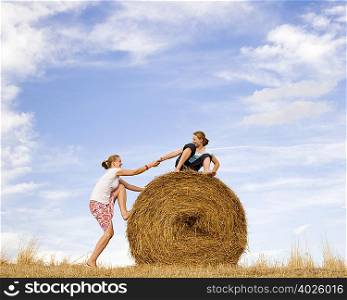 girl helping woman to climb hay bale