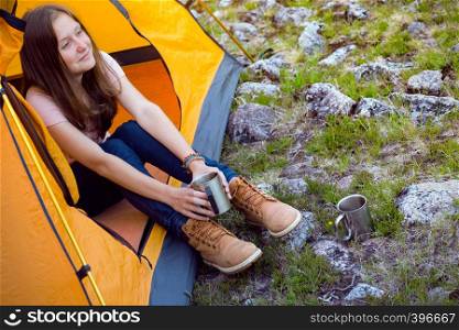 girl hiker in a tent and holding a cup mountains in the background
