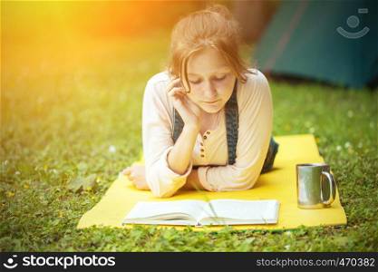 girl hiker lying and reading a book near the tent