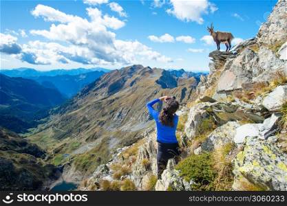 Girl hiker photographer ibex in the mountains on the rocks above a lake