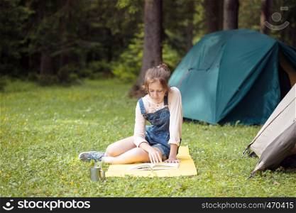 girl hiker sitting and reading a book near the tent