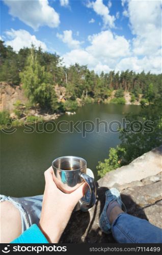 girl hiker sitting by the lake and holding a cup