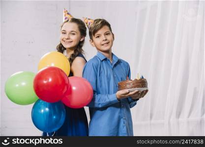 girl holding balloons boy holding birthday cake standing back back looking camera