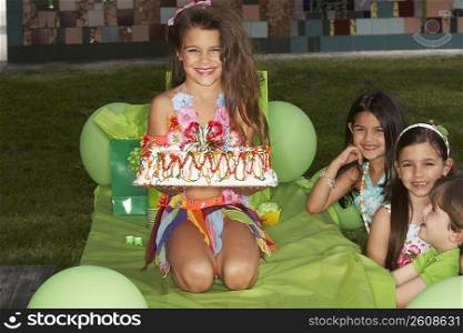 Girl holding birthday cake on a table at a birthday party with her three friends beside her