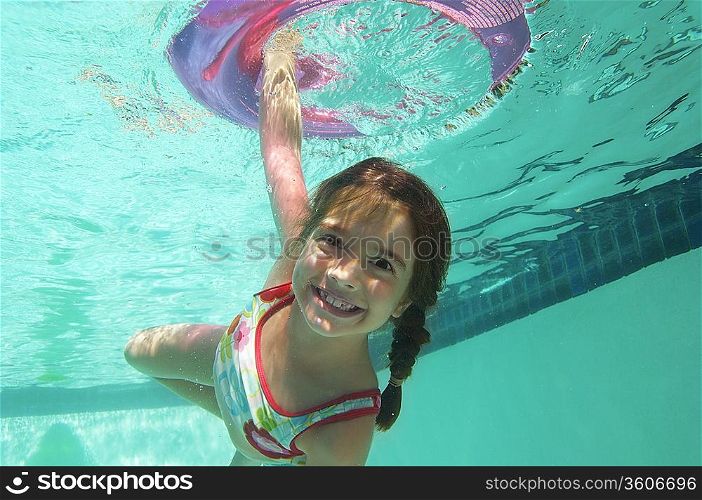 Girl holding inflatable raft underwater in swimming pool, portrait