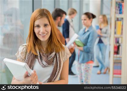Girl holding laptop with group of students in college library