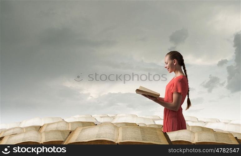 Girl holding opened book. Young woman in red dress with opened book in hand standing in pile of books
