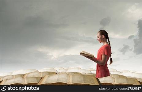 Girl holding opened book. Young woman in red dress with opened book in hand standing in pile of books