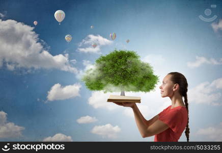 Girl holding opened book. Young woman in red dress with opened book in hand and green tree on pages