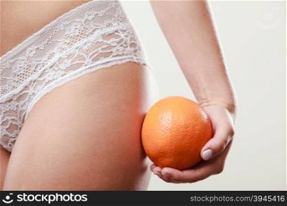 Girl holding orange next to bottom. Absence of cellulite. Part body of slim fit girl holding orange next to the bottom buttocks. Woman wearing white lacy lingerie. Diet aspects.