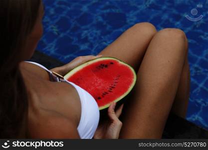 Girl holding watermelon near pool. Girl holding watermelon in the blue pool, slim legs. Tropical fruit diet. Summer holiday idyllic.