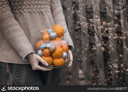 girl holds in her hands a jar of tangerines, nuts and Christmas balls. Christmas holidays
