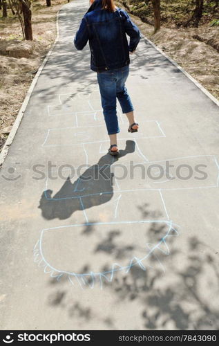 girl hopping in hopscotch on urban alley in sunny day