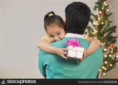 Girl hugs her dad while holding Christmas gift
