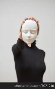 Girl in a black jumper hold gypsum mask sculpture instead of face on a white background, place for text. Concept The masks we wear.. Plaster mask in the hand of young female instead face on a white background, place for text. Concept The masks we wear.