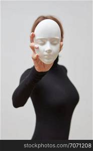 Girl in a black jumper hold plaster gypsum sculpture instead of face on a white background, place for text. Concept The masks we wear.. Young woman in a black sweater with plaster mask in her hand instead of face on a white background. Concept The masks we wear