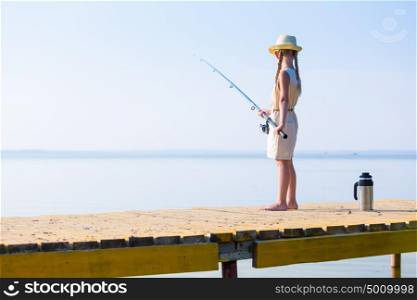 Girl in a dress and a hat with a fishing rod. Girl in a dress and a hat with a fishing rod fishing from the pier