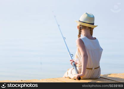 Girl in a dress and a hat with a fishing rod. Girl in a dress and a hat with a fishing rod fishing from the pier