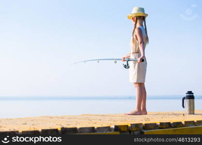 Girl in a dress and a hat with a fishing rod fishing from the pier